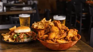 bowl of buffalo wings next to a burger and several glasses of beer