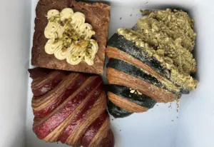 two large croissants, one red and one green, next to a blondie covered in frosting