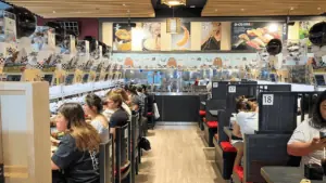 Guests dine at a revolving sushi restaurant with anime characters painted on the far wall.
