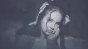 an blue-toned photo of lana del ray looking into the camera with one hand propped under her chin
