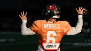 quarterback in an orange training jersey prepares to throw a football on the practice field