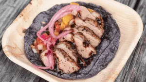 a blue corn tortilla on a plate. The tortilla is topped with onions, sliced and seasoned chicken, and green and yellow peppers.