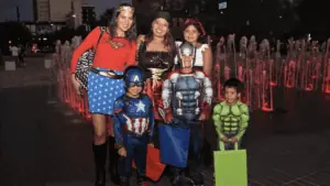 a group of people in super hero costumes pose in front of a fountain holding trick or treat bags