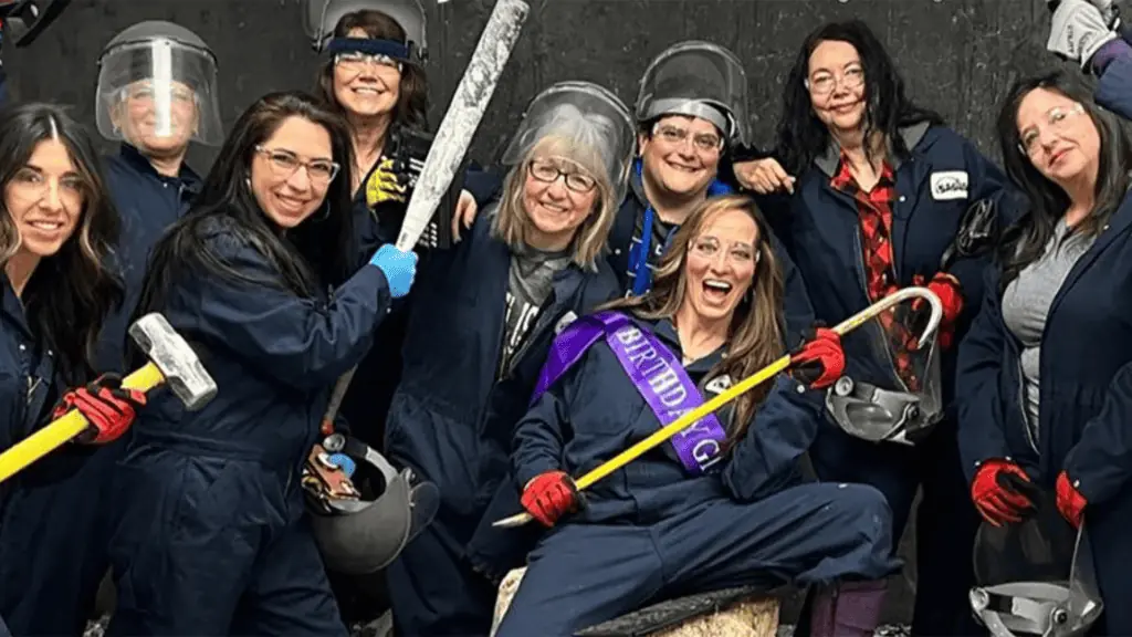 a group of people holding bats and hammers inside a smash room, a place where you can safely destroy a select number of items