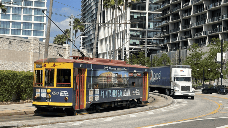 A streetcar riding through the heart of a downtown area. Tall buildings are visible in the background.