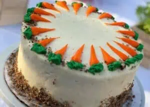 a large carrot cake with cream cheese frosting arranged on a white linen table cloth