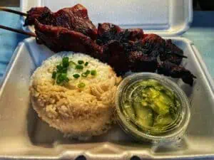 bbq pork on a plate with fried rice and a green dipping sauce
