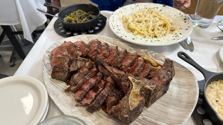 A steak and pasta dinner on a white table topped with white linen