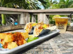 a plate of tacos on a drift wood table with a cocktail in plastic cup