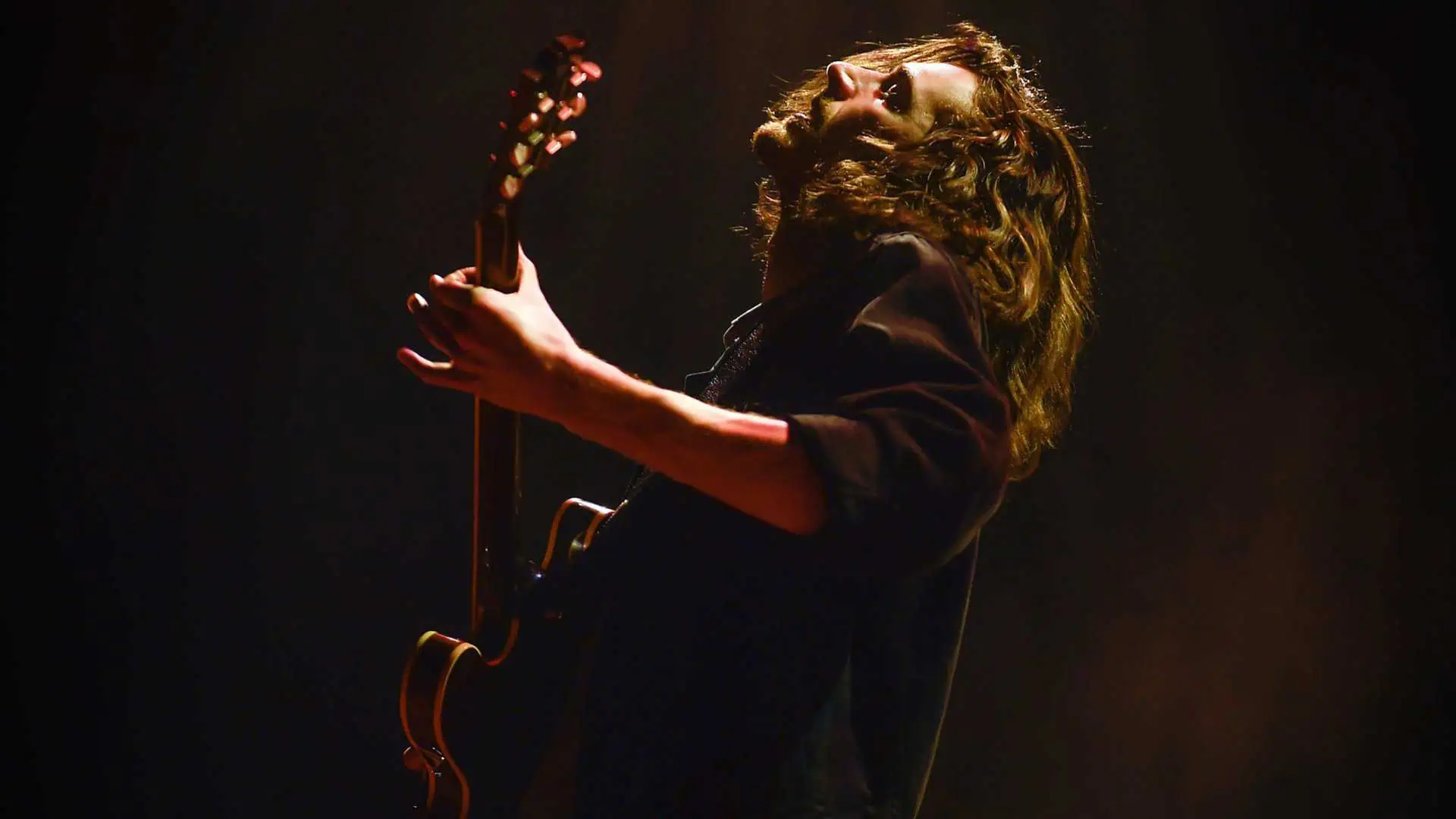 Hozier in profile tilts his face upward while playing guitar