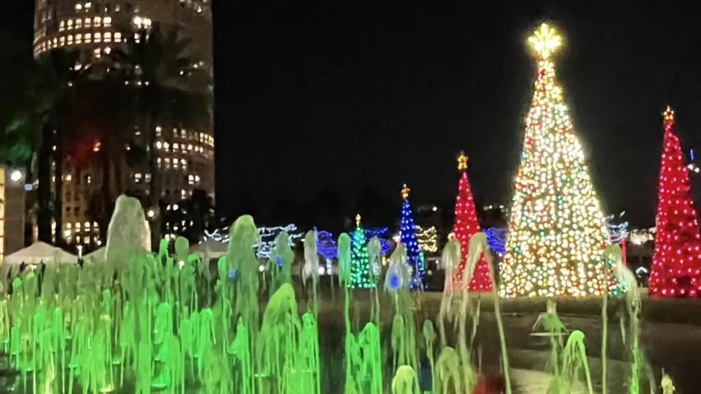 a park filled with Christmas lights. A Tree is lit and a colorful fountain spouts