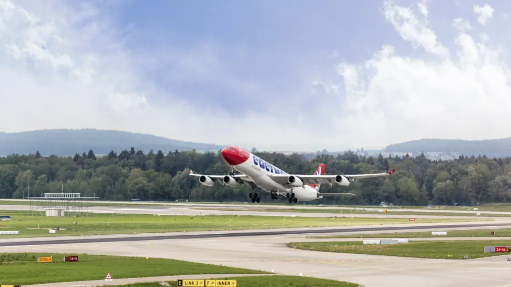 a plane taking off on the runway. Large hills can be seen in the background