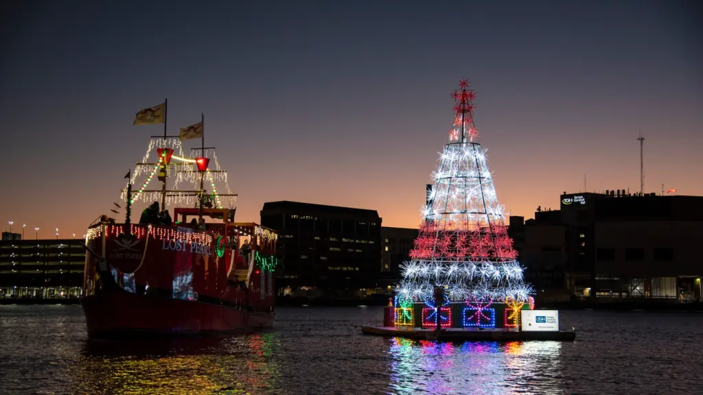 a floating Christmas tree next to a water taxi at sunset