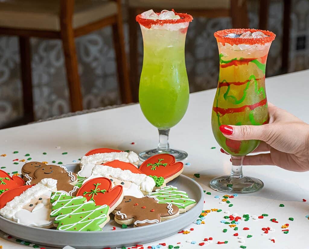 two green cocktails next to a plate of christmas cookies