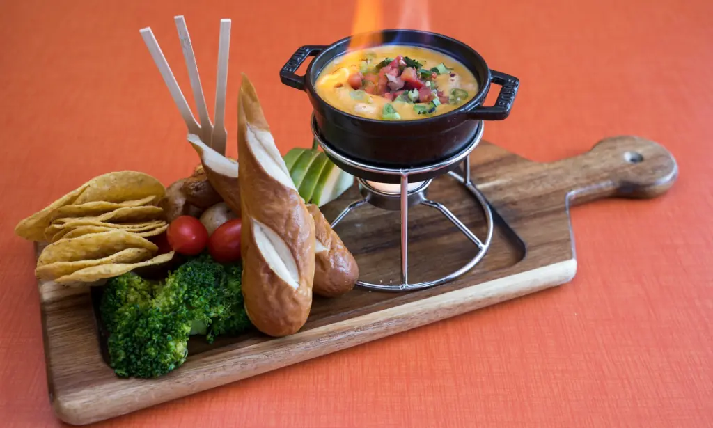 a bowl of fondue next to soft pretzels