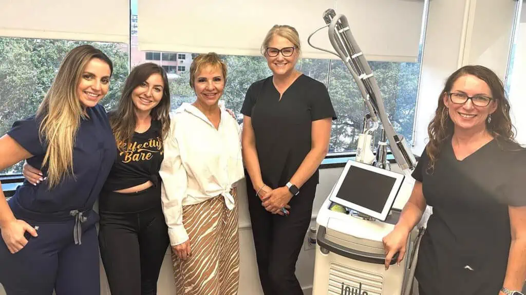 several staff members and the owner of Perfectly Bare Laser pose next to one of the treatment machines
