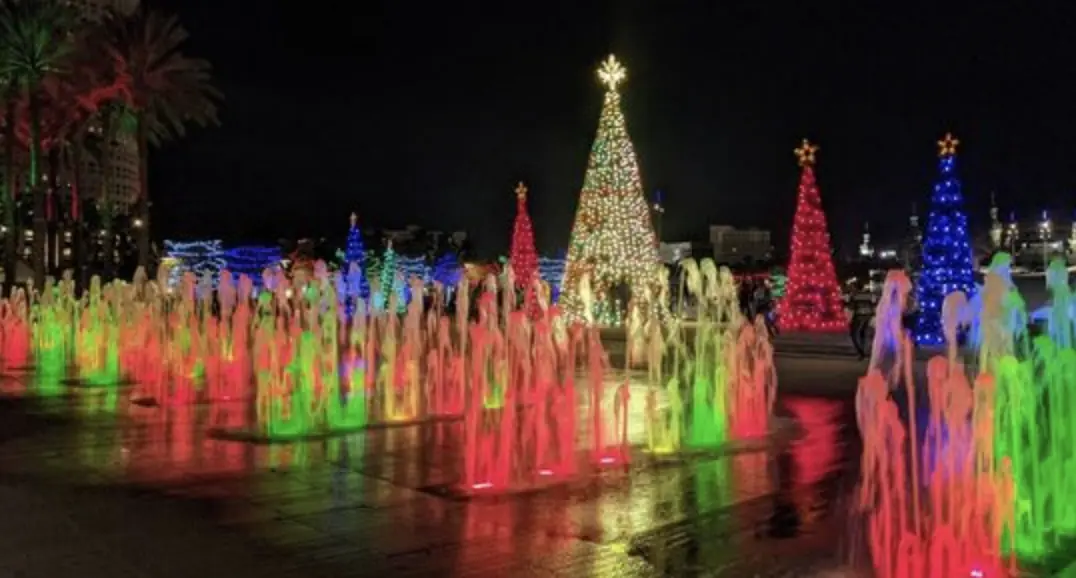 a colorful water fountain with christmas trees lit up in the background