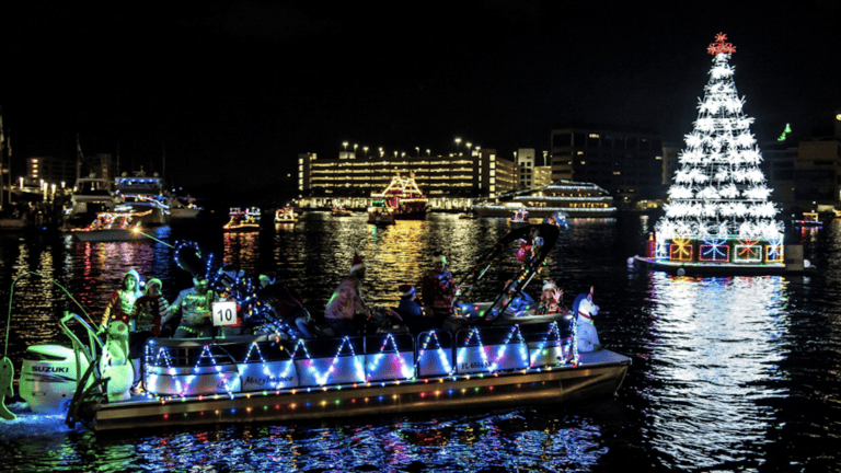 a lighted boat approaching a floating Christmas tree