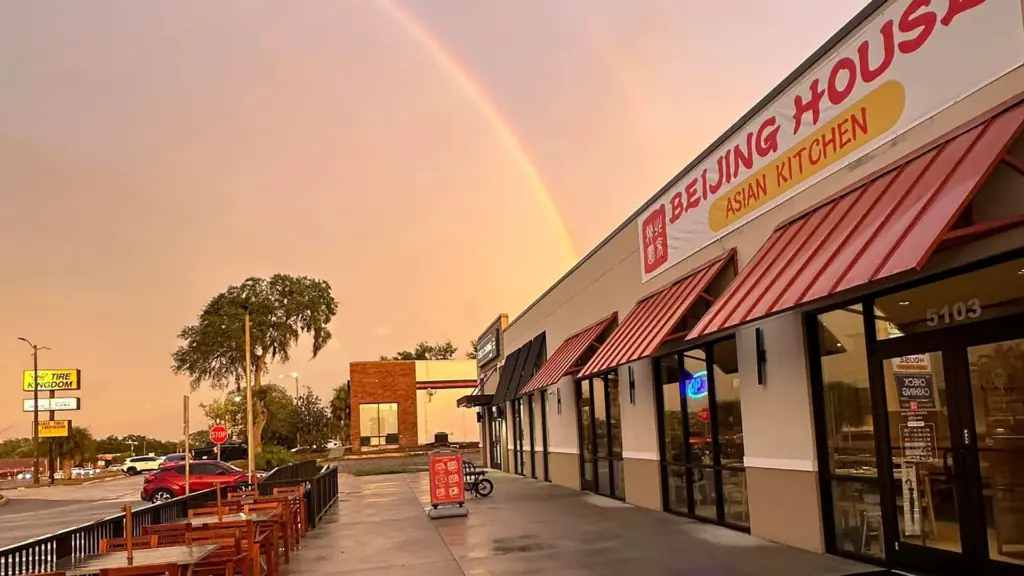 exterior of a restaurant with tables on the patio. A rainbow arches over the restaurant