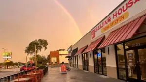 exterior of a restaurant with tables on the patio. A rainbow arches over the restaurant