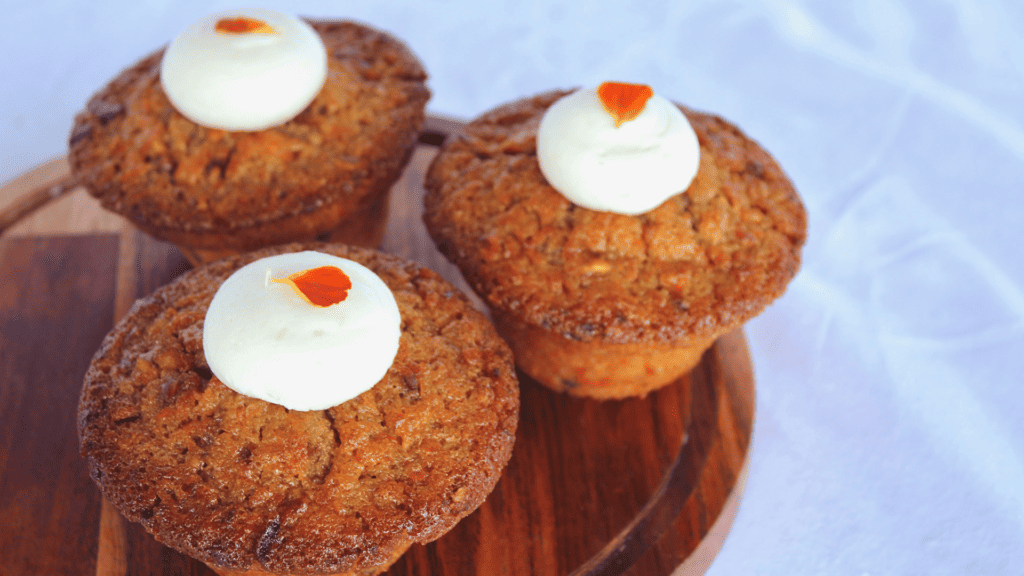 three carrot cake muffins on plate with cream cheese frosting on top
