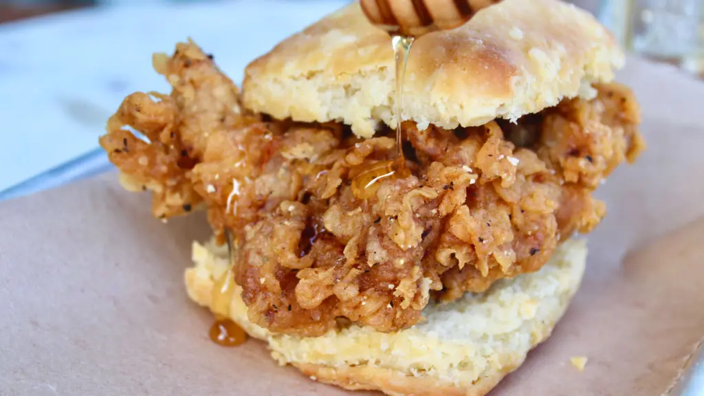 fried chicken sandwich served on a biscuit with honey dripping down the bun