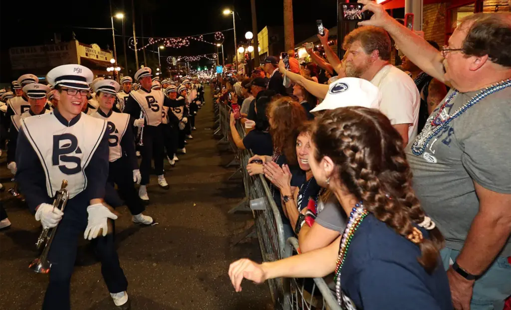 a marching band makes its way down the street as fans cheer