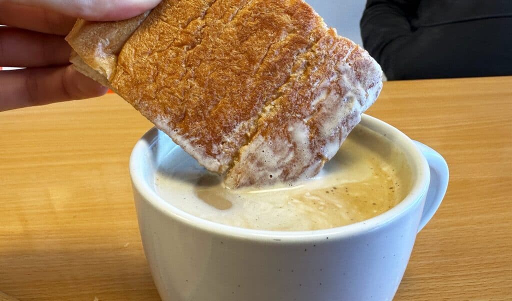 a piece of toast being dipped into a cup of coffee