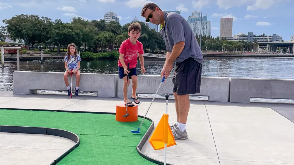 a father and two of his children play mini golf on pier