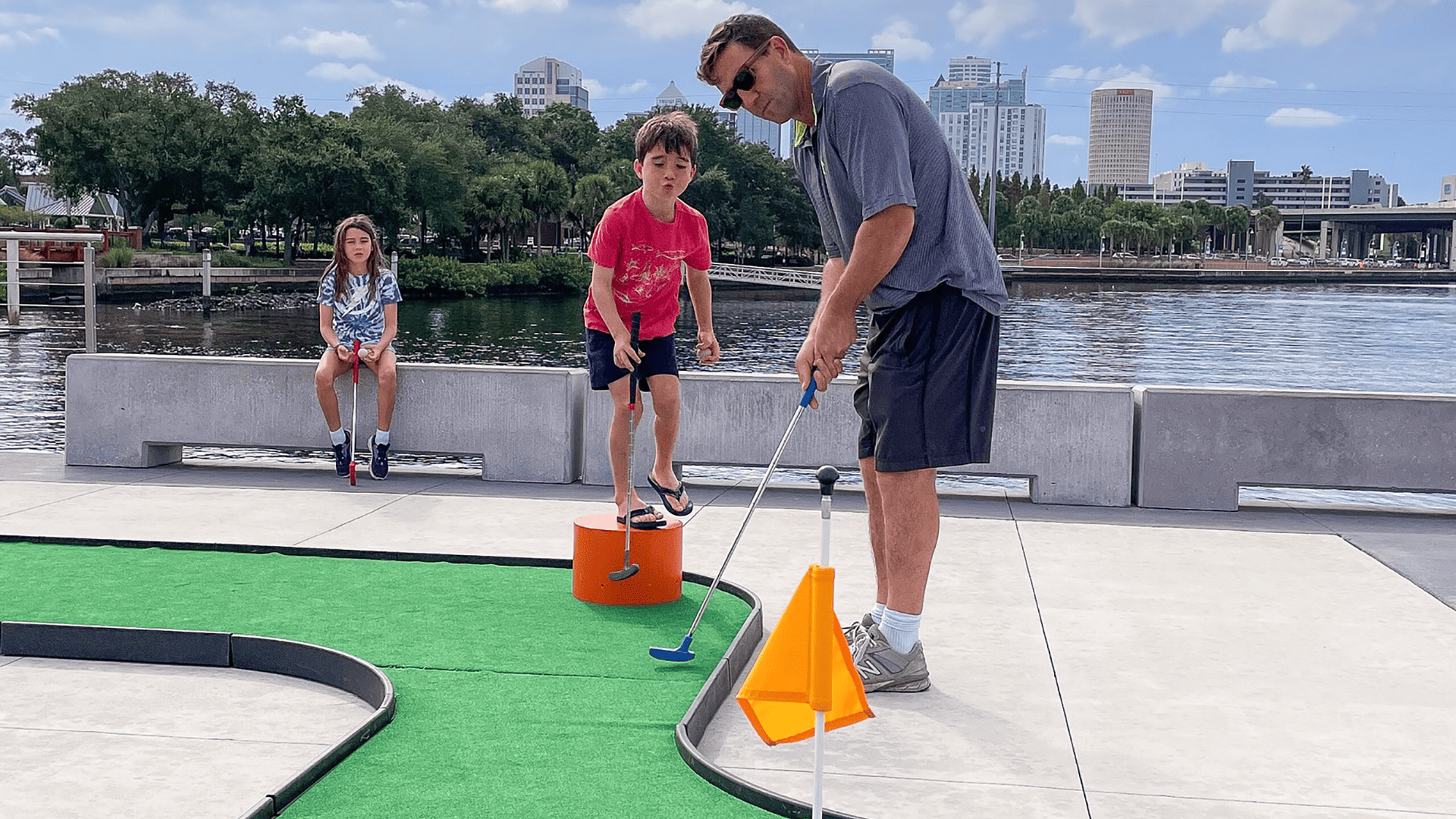 a father and two of his children play mini golf on pier