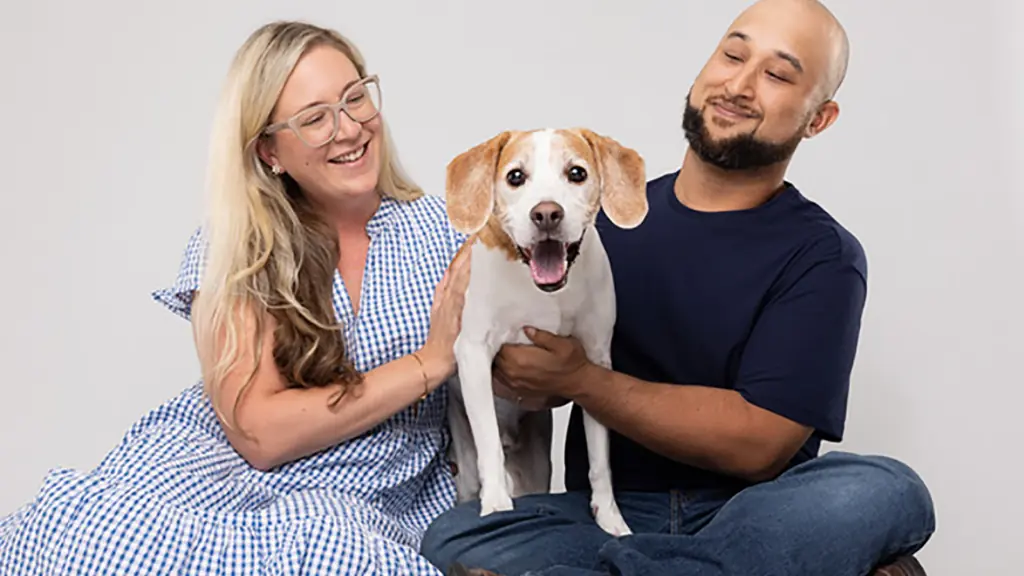 Two people sit with their dog in a photo studio