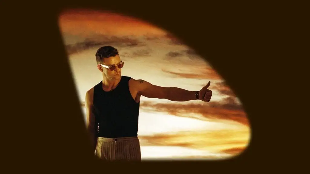 Justin Timberlake poses against an orange background. He's wearing orange sunglasses and a tank top and pin stripe pants