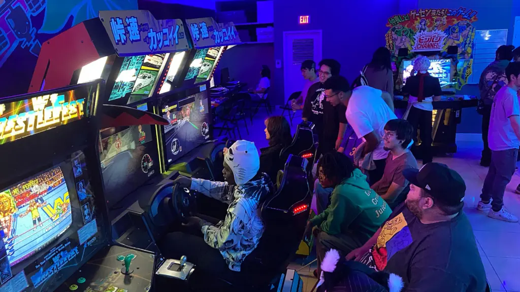 a group of people gather around a racing game at an arcade