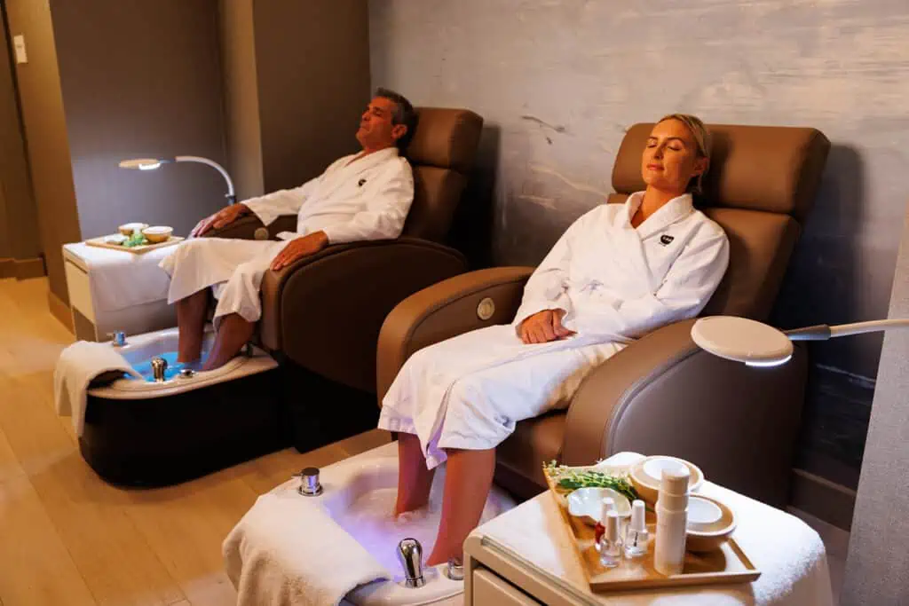 two people sitting in leather lounge chairs in bathrobes enjoying a spa day