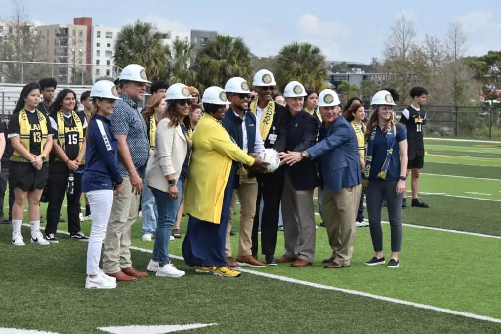 A group of city officials wear hard hats, and officially break ground on a new soccer field
