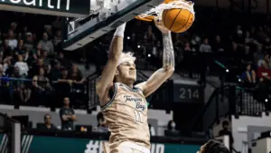 a basketball player dunks. He's wearing a gold and green jersey