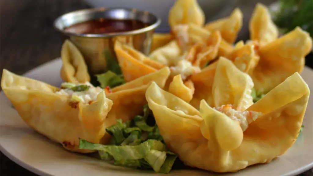 a plate of crab Rangoons with sauce dishes on the side