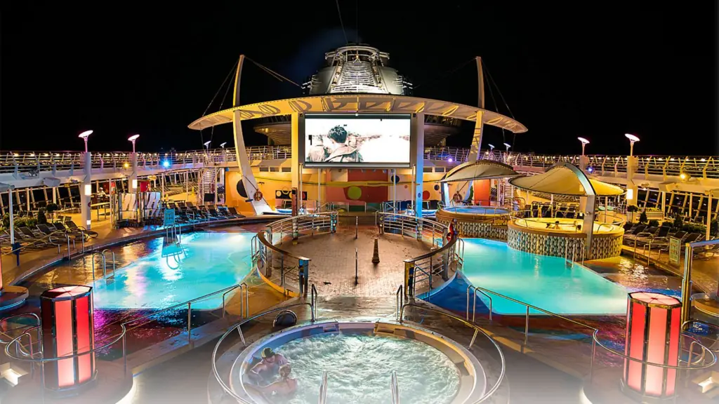 two pools on either side of a large cruise ship at night. A big screen has a film projected on it. 