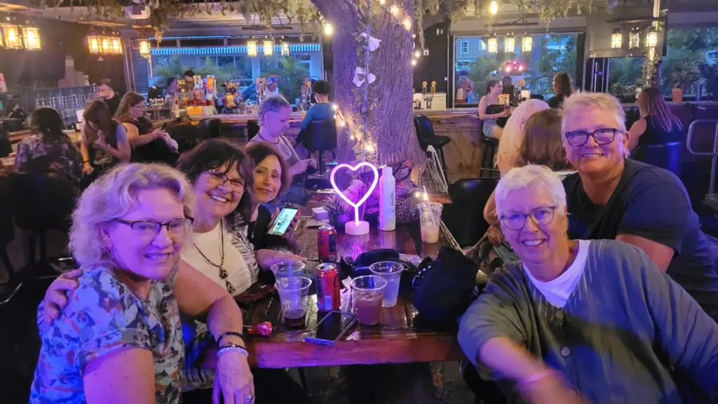 a group of people at an outdoor bar. There's a heart-shaped neon sculpture on the table