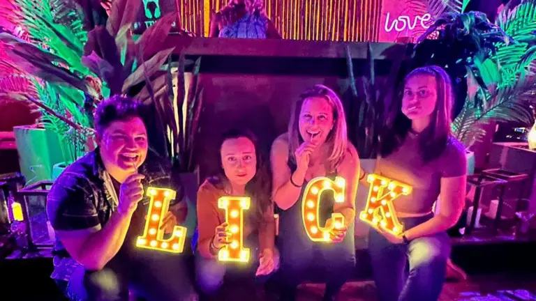 four people hold up glowing letters that spell out "LICK"