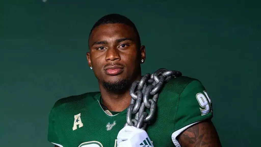 a football player in a green journey poses with a large chain over his shoulder