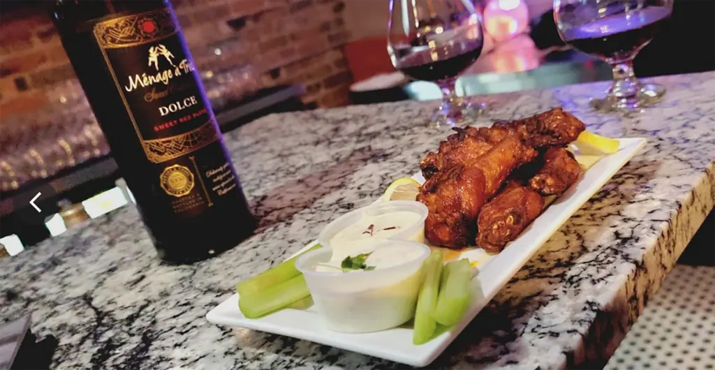 a plate of chicken wings next to a bottle of wine