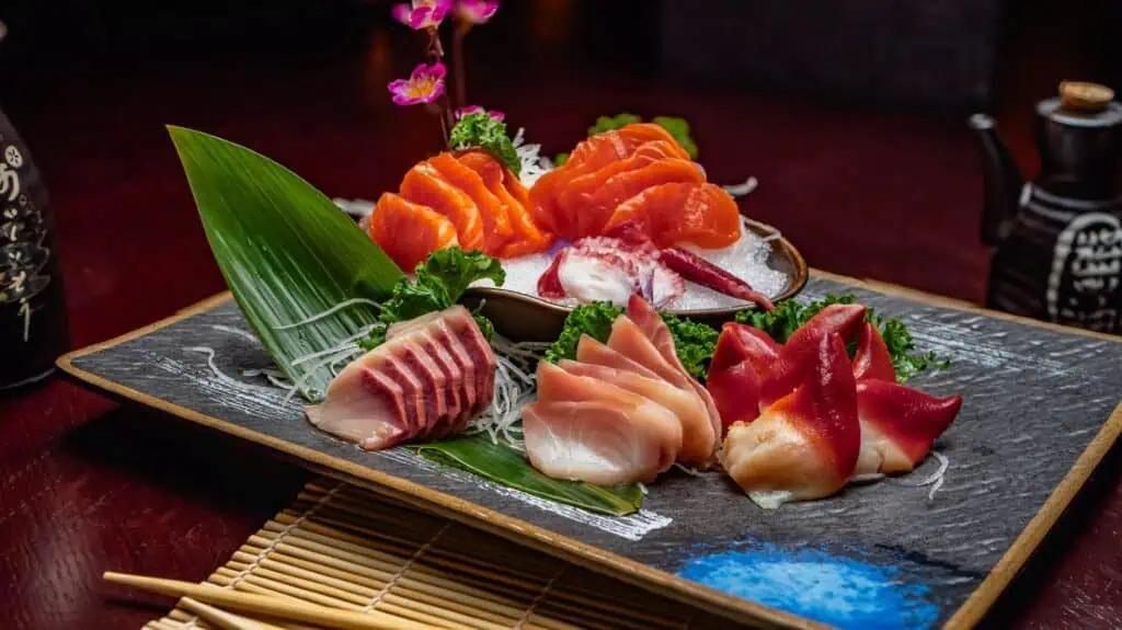 sashimi platter beautifully arranged on a black plate and brown table -- soy sauce in background