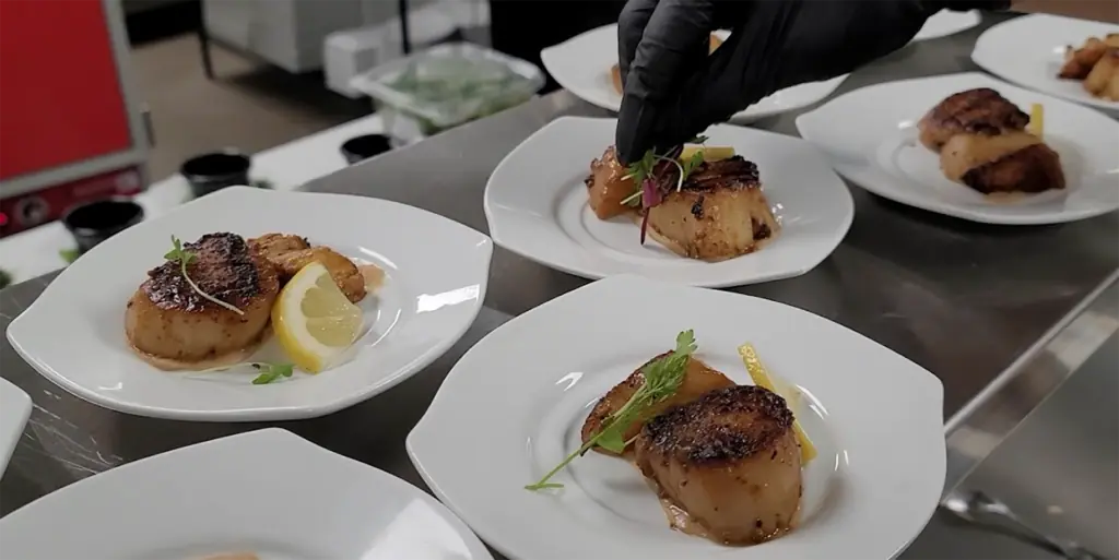 sea scallops being plated with greens 