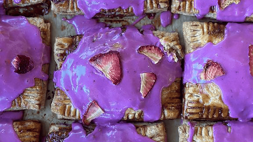 Aerial view of pop tart covered in purple frosting and topped with sliced strawberry