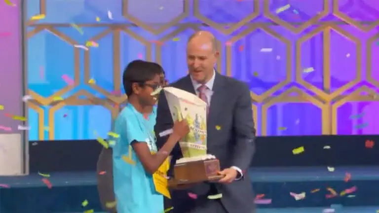 A young person receives a trophy on stage during a spelling bee