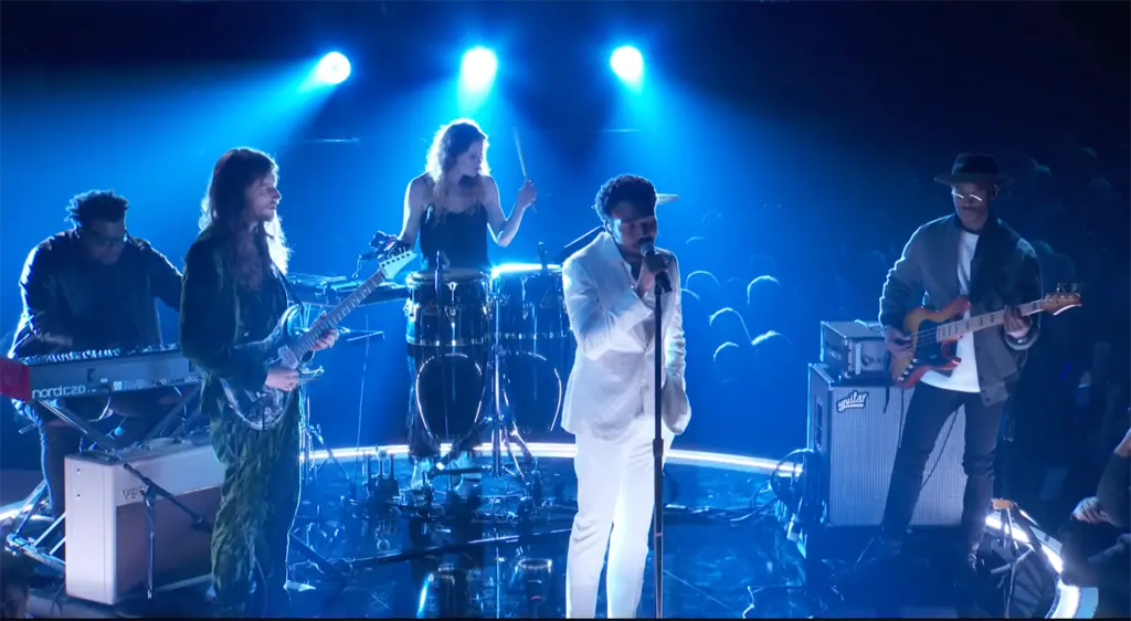 a singer on stage in a white suit performs with a band around him