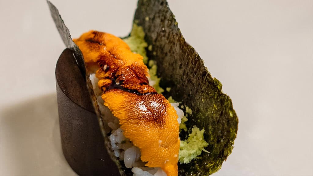 a sushi hand roll with orange sauce on top
