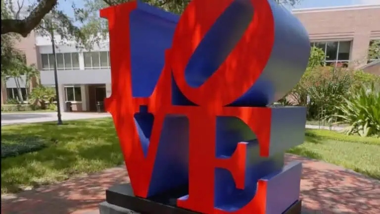 a large LOVE sculpture with red and blue tones set on a college campus.