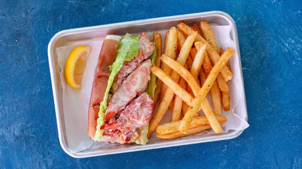 a lobster roll on a plate with fries 